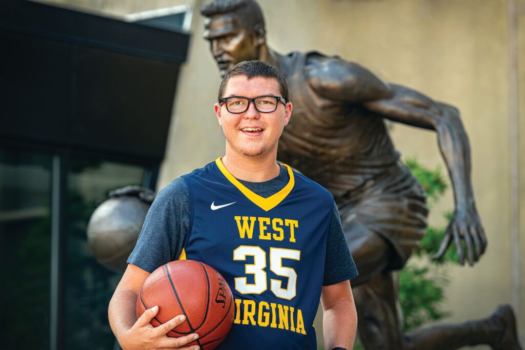 Joe Runnels, basketball fan and 18-year-old pediatric epilepsy patient being treated at WVU RNI by WVU Medicine's Dr. Ali Rezai, executive chair of the Rockefeller Neuroscience Institute poses with WVU basketball legend Jerry West at the WVU Coliseum Evan